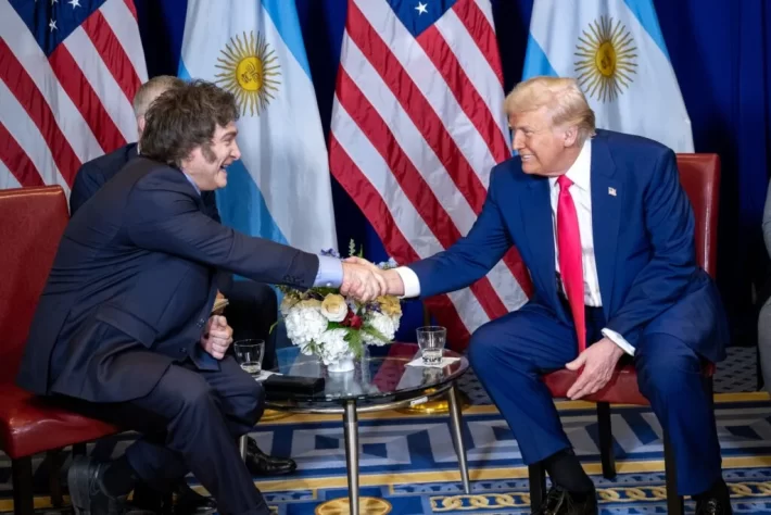 Donald Trump and Javier Milei sitting shaking hands.